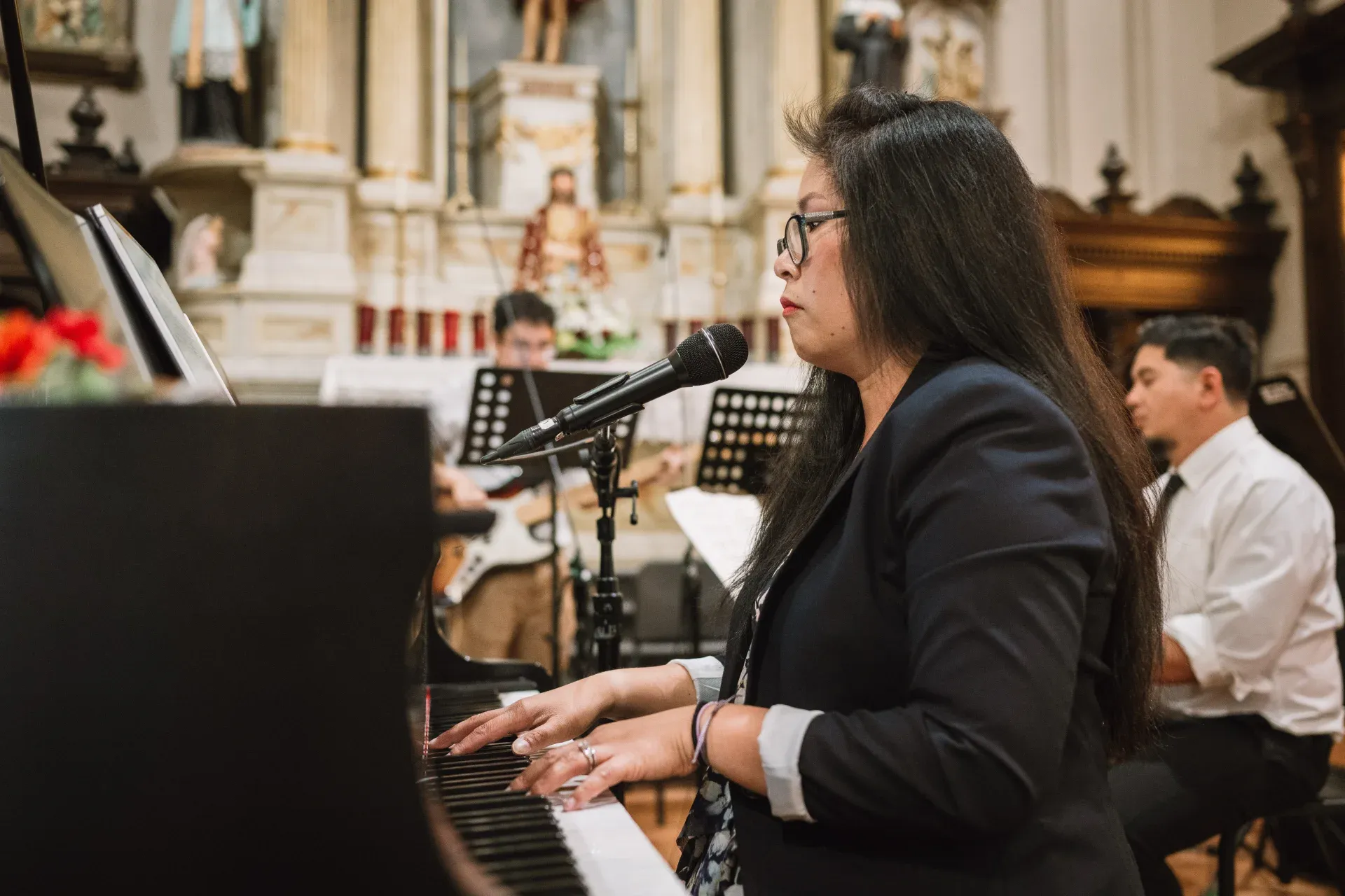 Anhthu at a grand piano with a small ensemble before the altar of a sunlit church