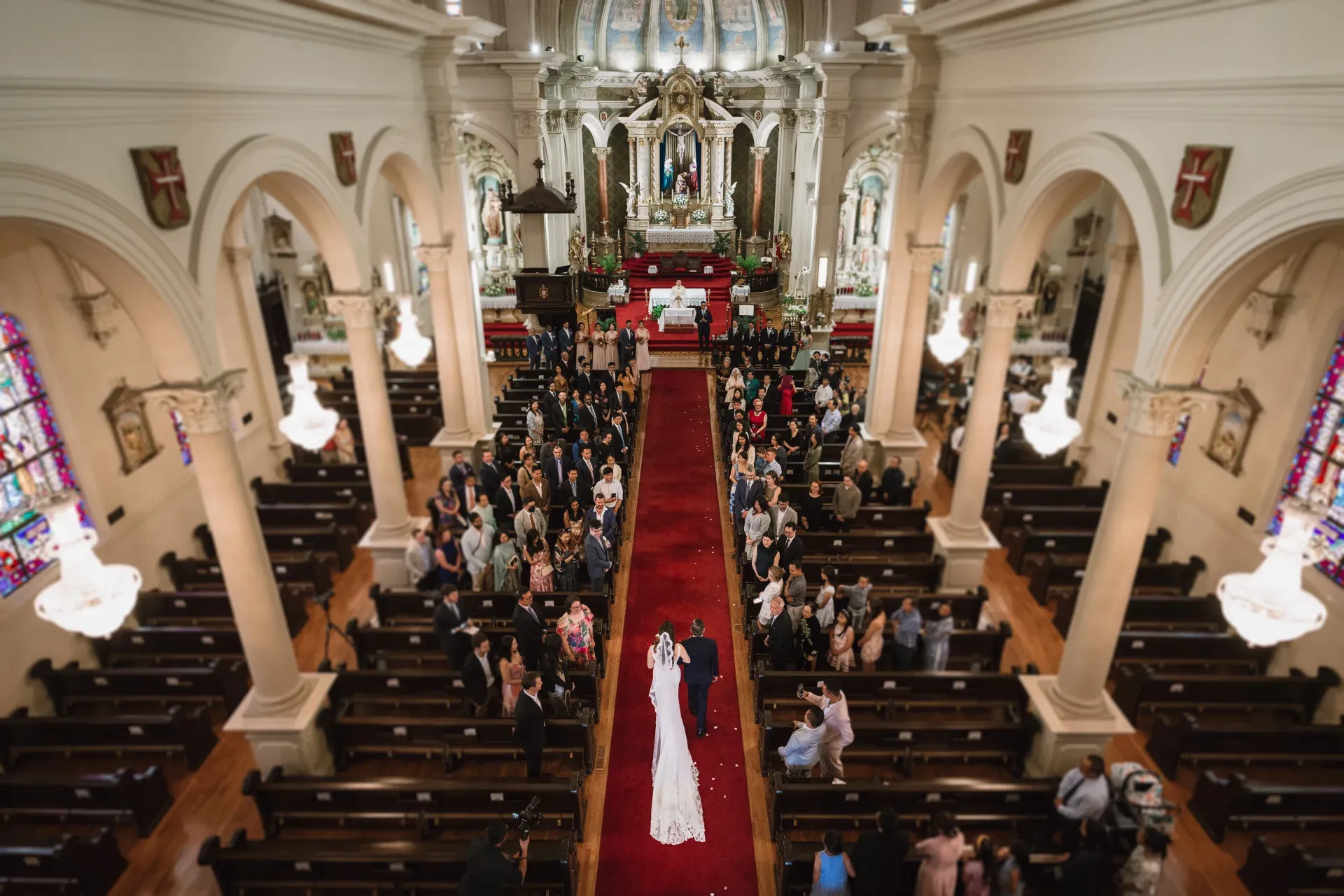 A Catholic wedding from the choir loft: the bride walking the red aisle of a full church toward the altar